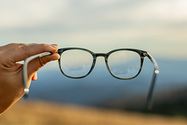 Reading glasses are held in front of a blue sky.