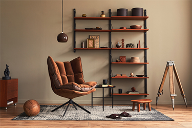 An empty brown chair rests on a blue carpet in front of black and brown shelves containing pottery.