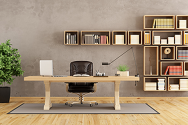 An empty chair sits at a wooden desk in an office. Behind those are shelves containing books.