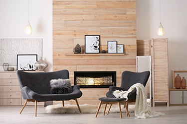 Two empty black chairs are in front of a fireplace set in a wood-paneled wall.