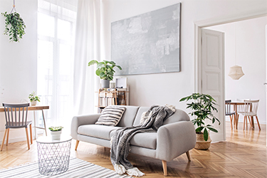 Modern Scandinavian living room with design sofa featuring elegant blanket, coffee table and bookstand on a white wall. Brown wooden parquet. Concept of minimalistic interior.