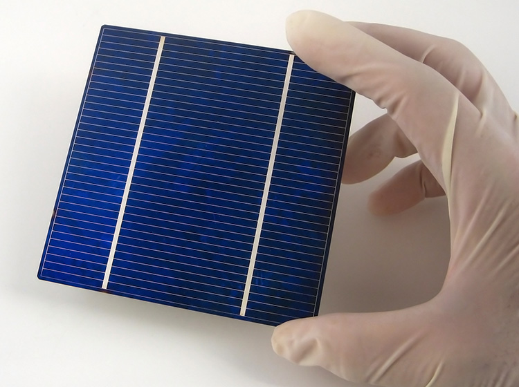 A researcher with protective gloves holds a solar panel module.