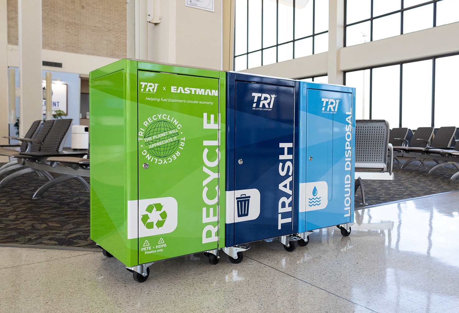 A recycling receptacle in an airport terminal is green and is marked Tri Recycling in white letters.  A recycling receptacle in an airport terminal is green and is marked Tri Recycling in white letters.