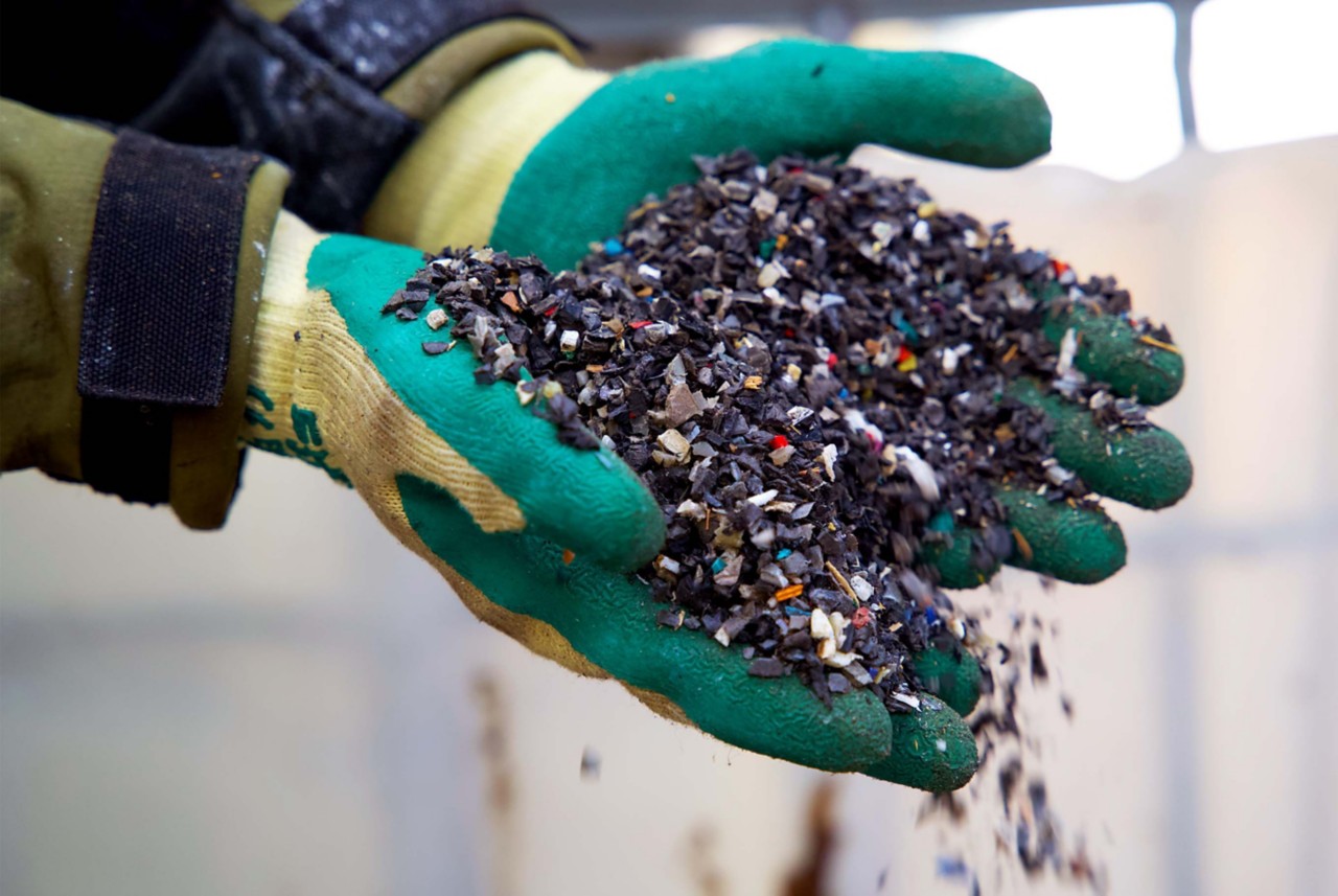 A pair of gloved hands holding a colorful pile of automotive shredder residue. A pair of gloved hands holding a colorful pile of automotive shredder residue.