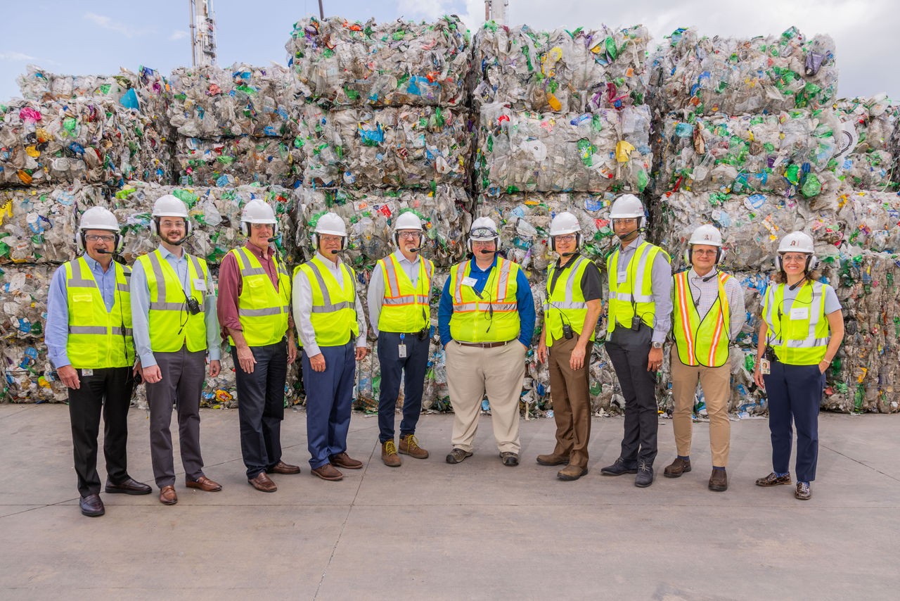 Steven Cook, Kevin McOmber, EPA staff and Eastman team members wear protective gear in front of bales of plastic waste. Steven Cook, Kevin McOmber, EPA staff and Eastman team members wear protective gear in front of bales of plastic waste.