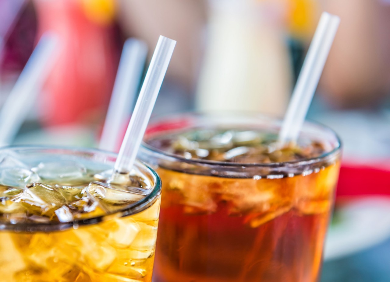 Straws sit in clear glasses filled with ice and a drink 