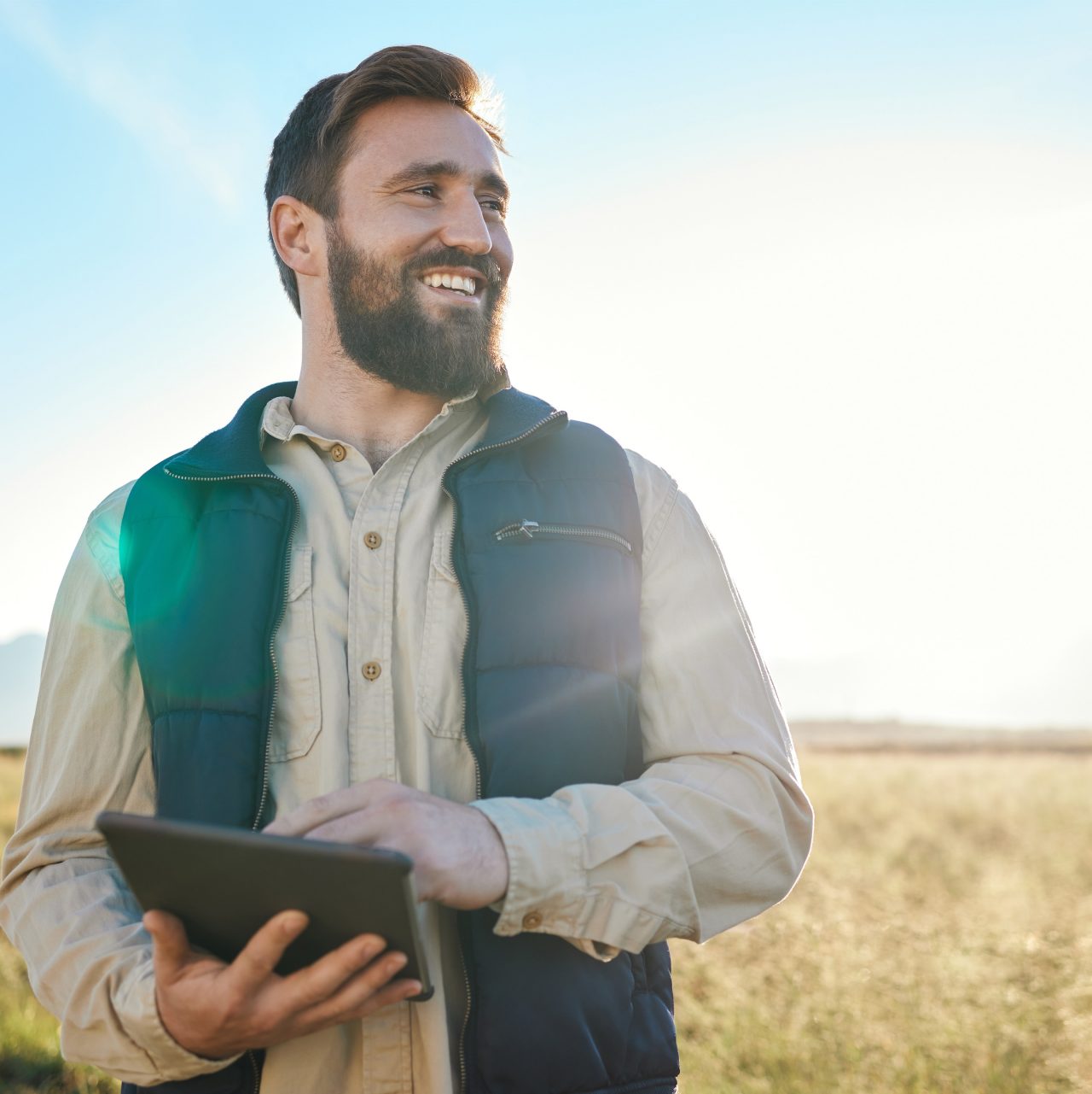 A person holds a tablet computer while standing in a field.  