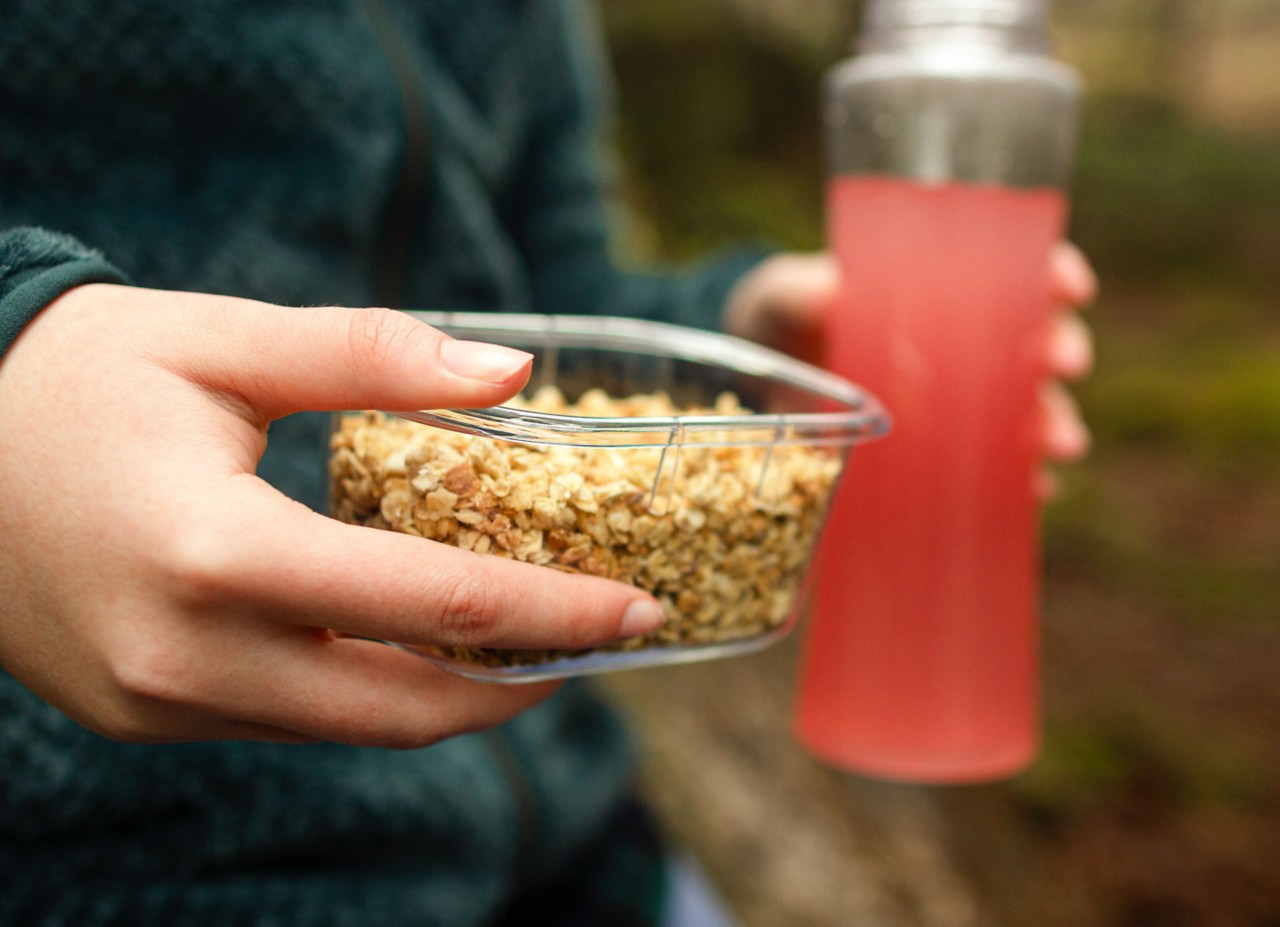 Close-up of a person holding a small food storage container in one hand and a drink bottle in the other.