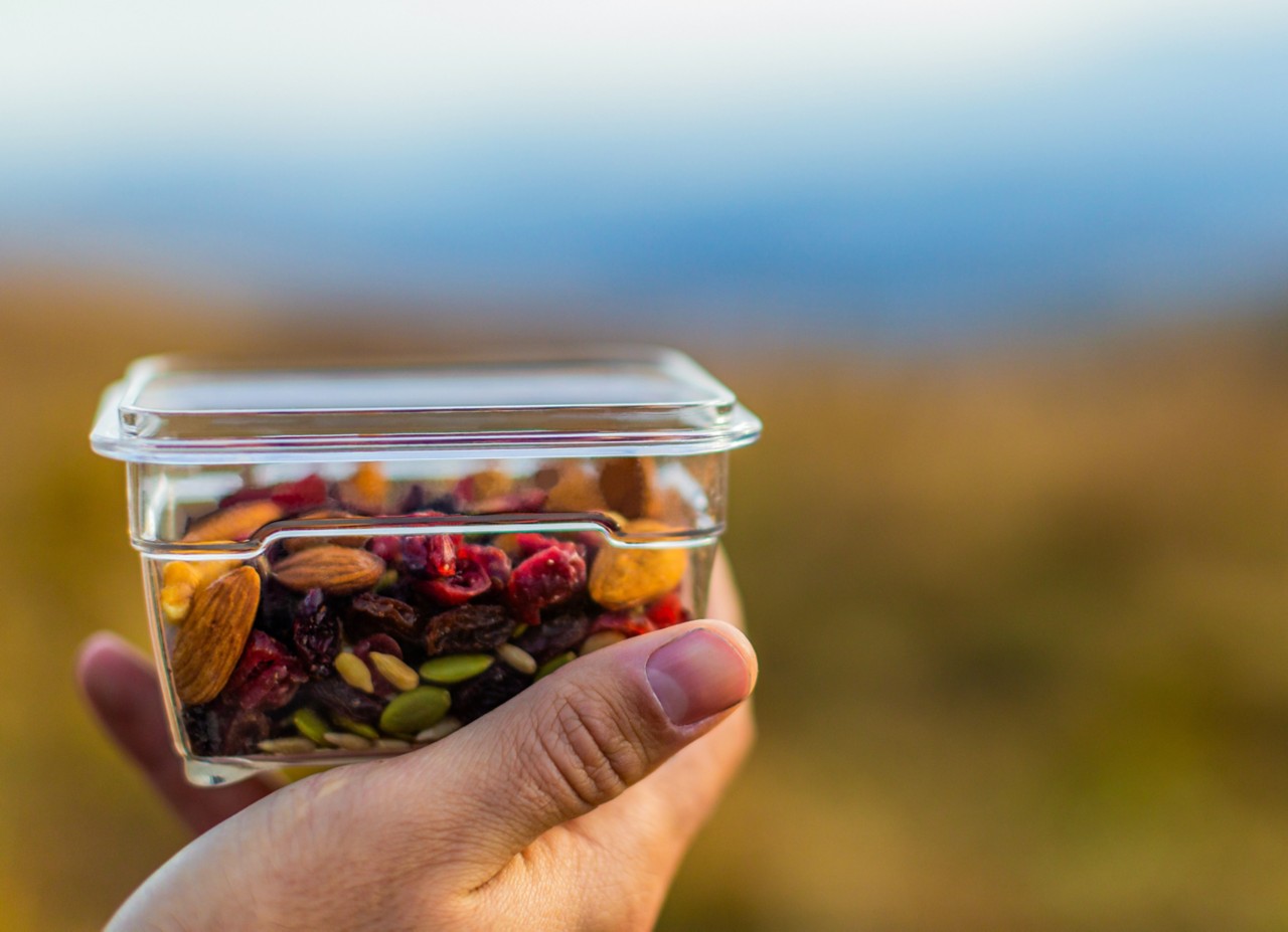 Close-up of a hand holding a storage container with snack mix in it.