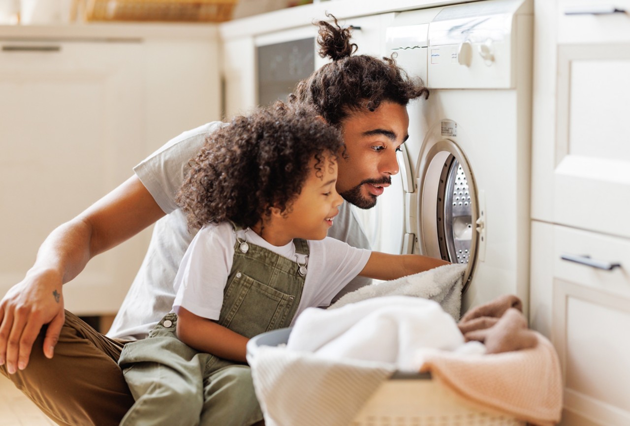 Son helping dad to load washing machine. 