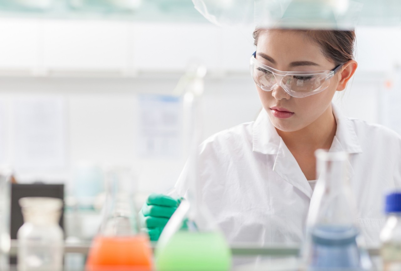 A scientist wearing safety goggles, a lab coat, and gloves in the laboratory. 