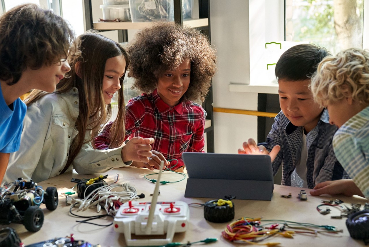 Children looking at various electronics and a laptop on a table. 