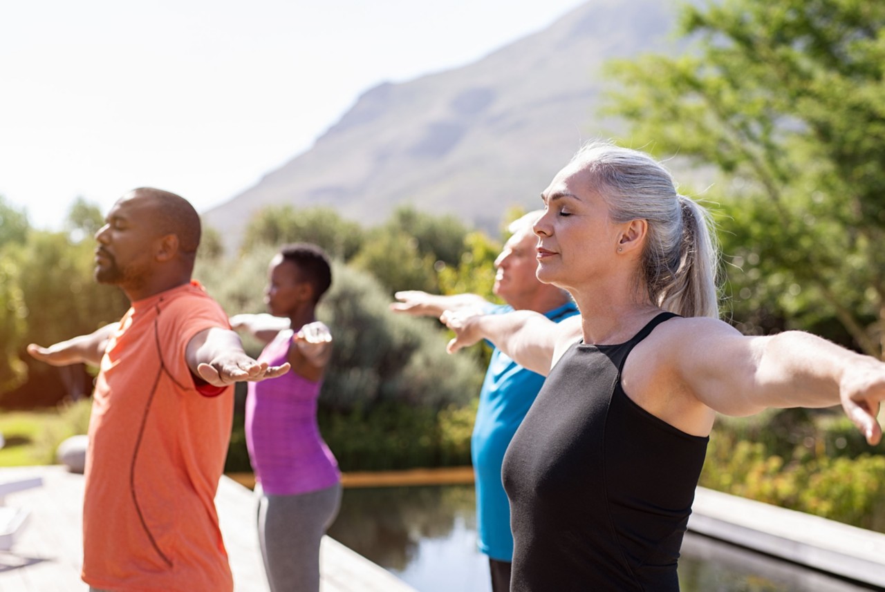 Un grupo de personas practica yoga al aire libre bajo el sol 